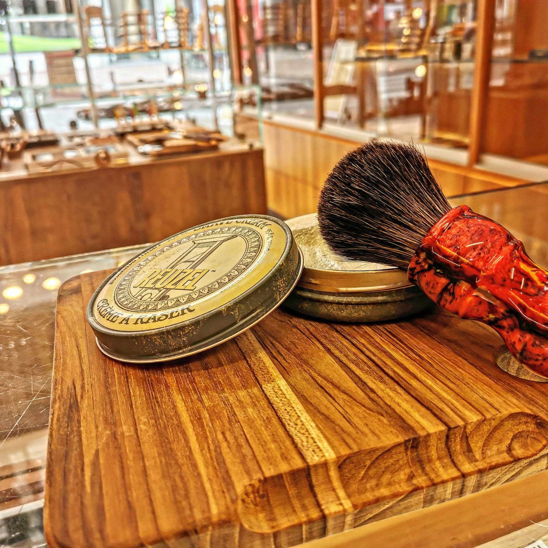 Savon à raser en boîte de laiton et blaireau posés sur une planche en bois, en boutique
